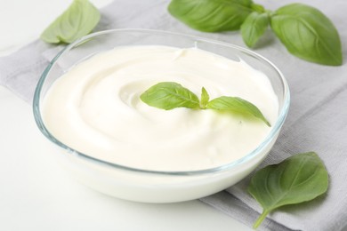 Photo of Tasty yoghurt with basil in bowl on white table, closeup