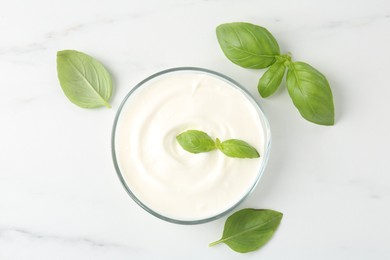 Photo of Tasty yoghurt with basil in bowl on white marble table, flat lay