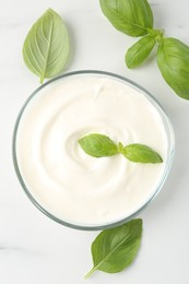 Photo of Tasty yoghurt with basil in bowl on white table, flat lay