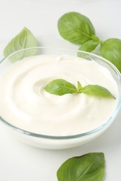 Photo of Tasty yoghurt with basil in bowl on white table, closeup