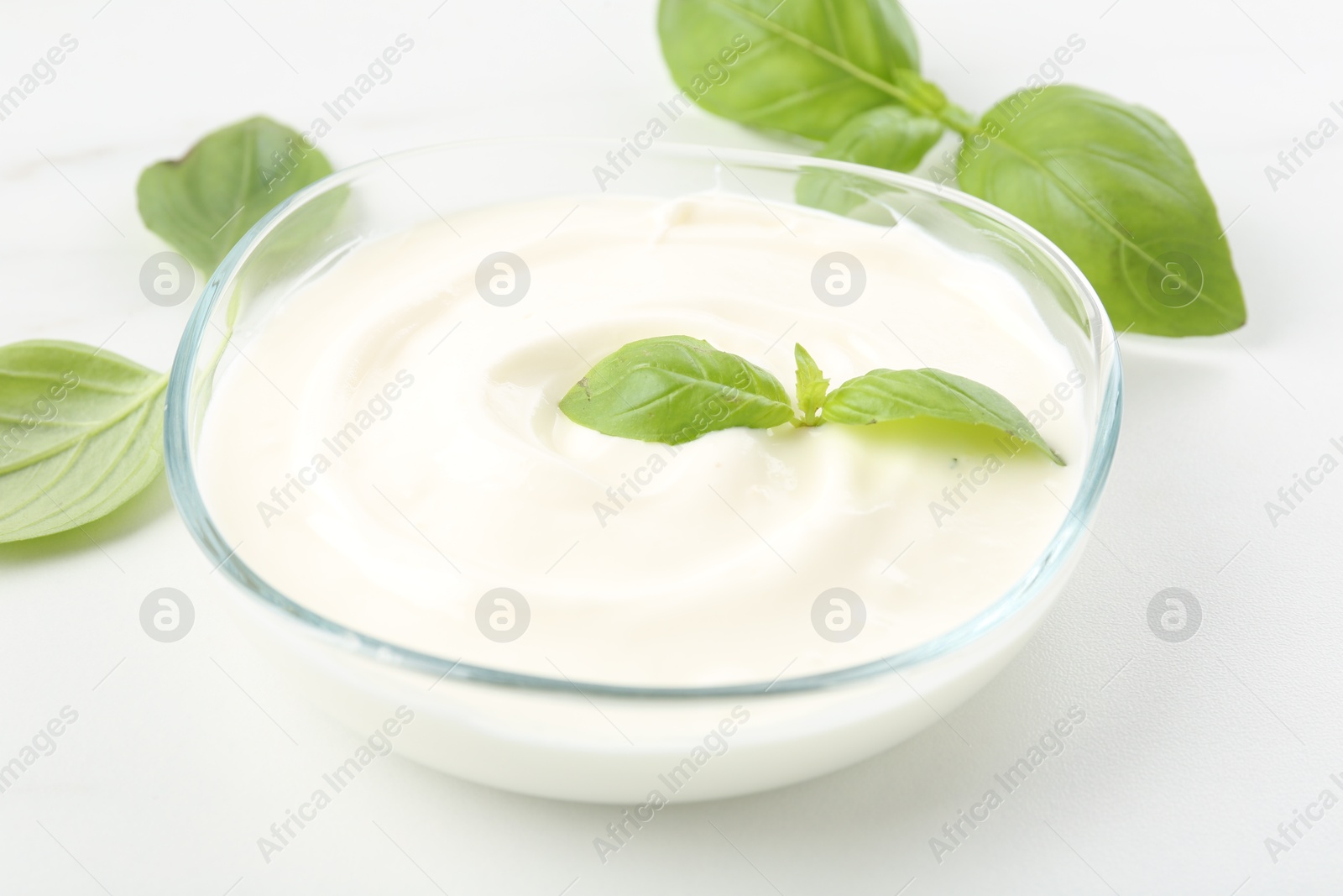 Tasty yoghurt with basil in bowl on white table, closeup Photo of Tasty yoghurt with basil in bowl on white table, closeup