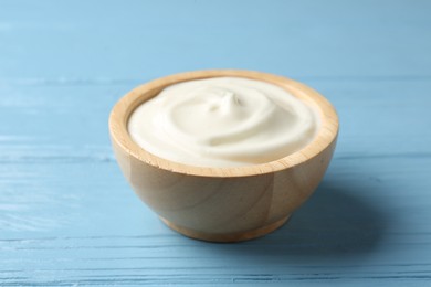 Photo of Tasty yoghurt in bowl on light blue wooden table, closeup