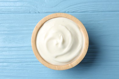 Photo of Tasty yoghurt in bowl on light blue wooden table, top view