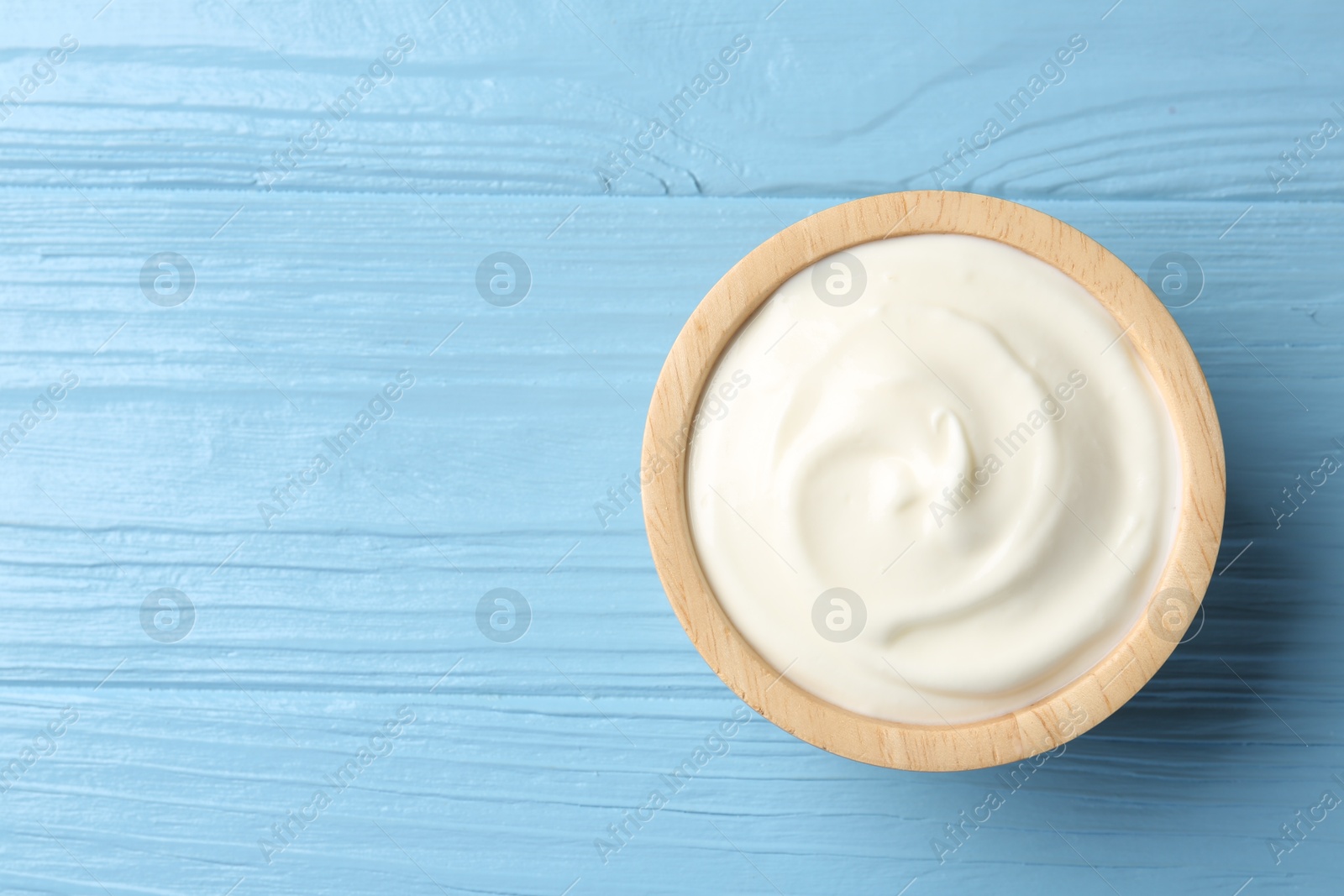 Tasty yoghurt in bowl on light blue wooden table, top view. Space for text Photo of Tasty yoghurt in bowl on light blue wooden table, top view. Space for text