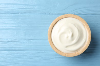Photo of Tasty yoghurt in bowl on light blue wooden table, top view. Space for text