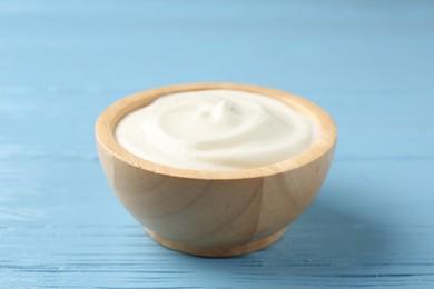 Photo of Tasty yoghurt in bowl on light blue wooden table, closeup