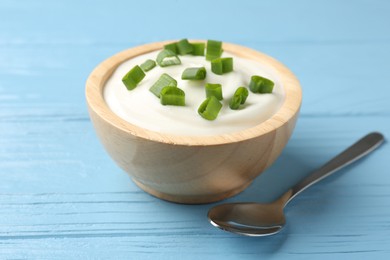 Photo of Tasty yoghurt with green onions in bowl on light blue wooden table, closeup