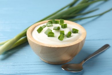 Photo of Tasty yoghurt with green onions in bowl on light blue wooden table, closeup