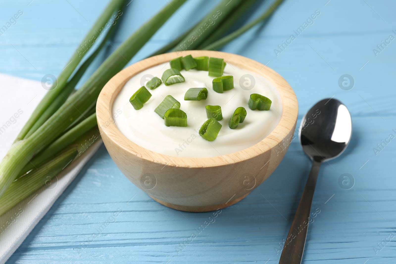 Photo of Tasty yoghurt with green onions in bowl on light blue wooden table, closeup