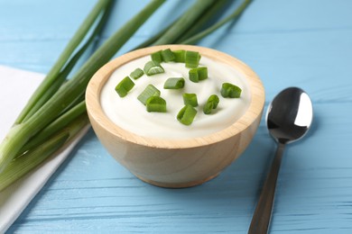 Photo of Tasty yoghurt with green onions in bowl on light blue wooden table, closeup