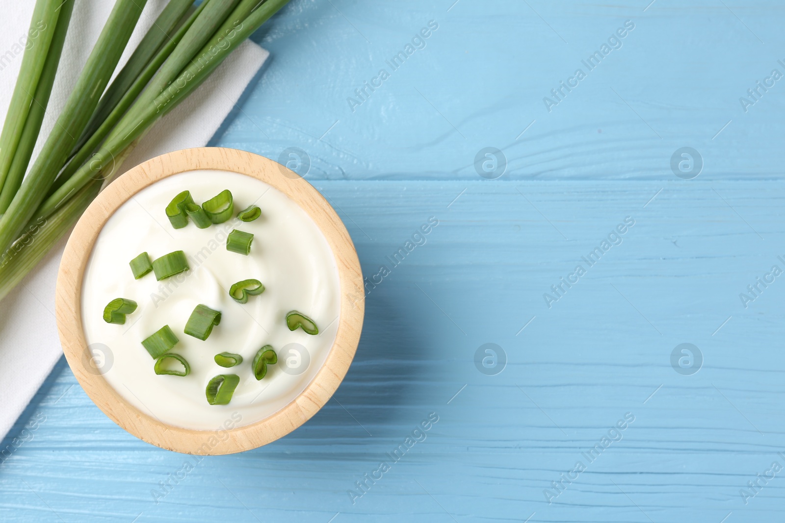 Photo of Tasty yoghurt with green onions in bowl on light blue wooden table, flat lay. Space for text