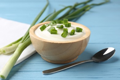 Photo of Tasty yoghurt with green onions in bowl on light blue wooden table, closeup
