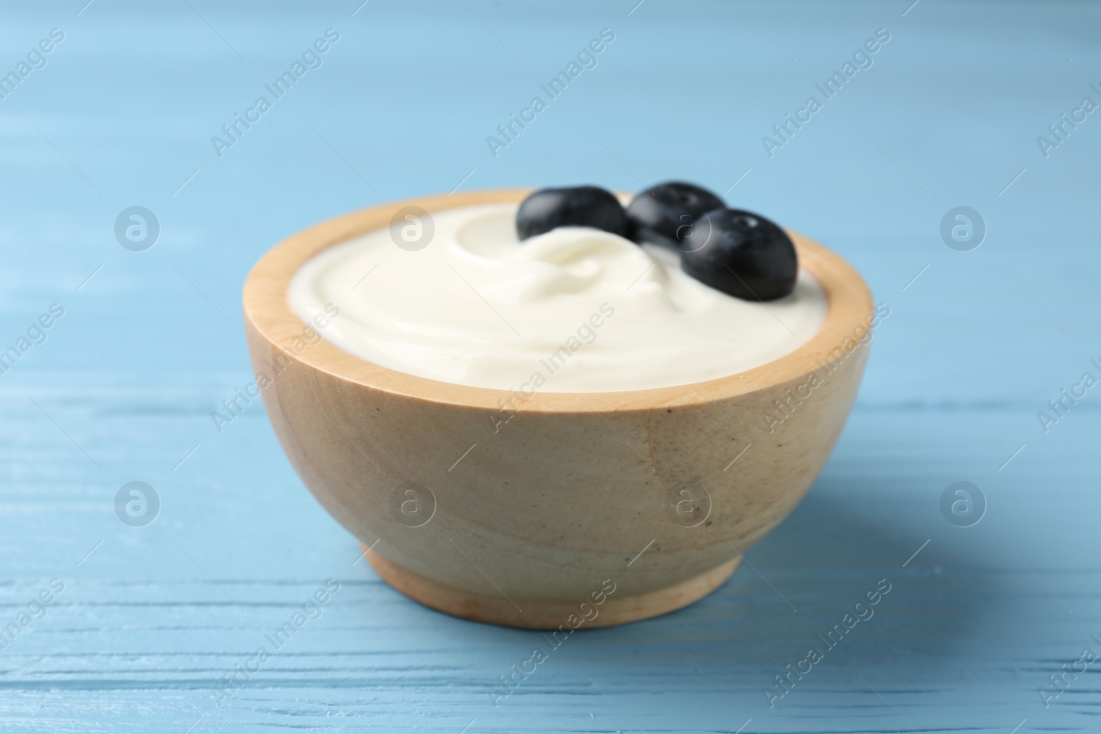 Photo of Tasty yoghurt with blueberries in bowl on light blue wooden table, closeup