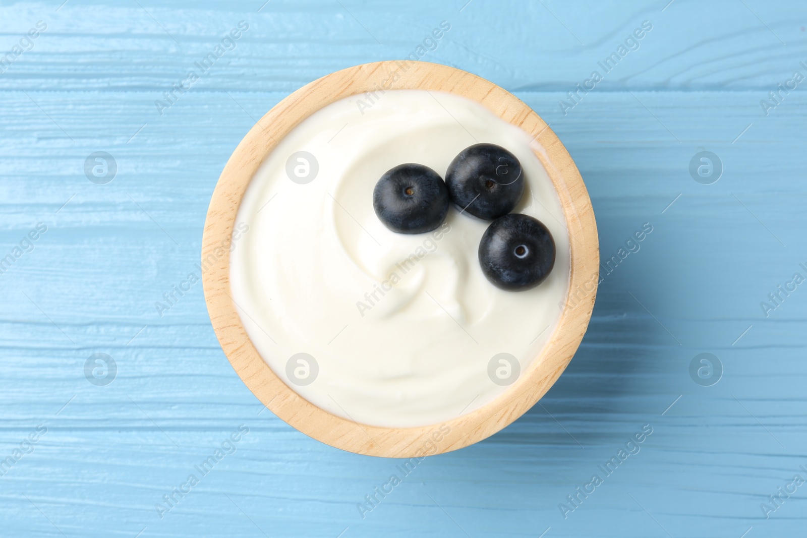 Photo of Tasty yoghurt with blueberries in bowl on light blue wooden table, top view