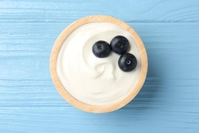 Photo of Tasty yoghurt with blueberries in bowl on light blue wooden table, top view