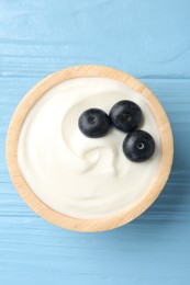 Photo of Tasty yoghurt with blueberries in bowl on light blue wooden table, top view