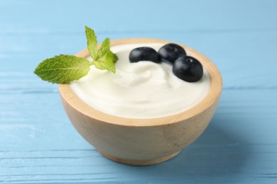 Photo of Tasty yoghurt with blueberries and mint in bowl on light blue wooden table, closeup