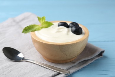 Photo of Tasty yoghurt with blueberries and mint in bowl on light blue wooden table, closeup