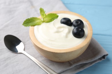 Photo of Tasty yoghurt with blueberries and mint in bowl on light blue wooden table, closeup