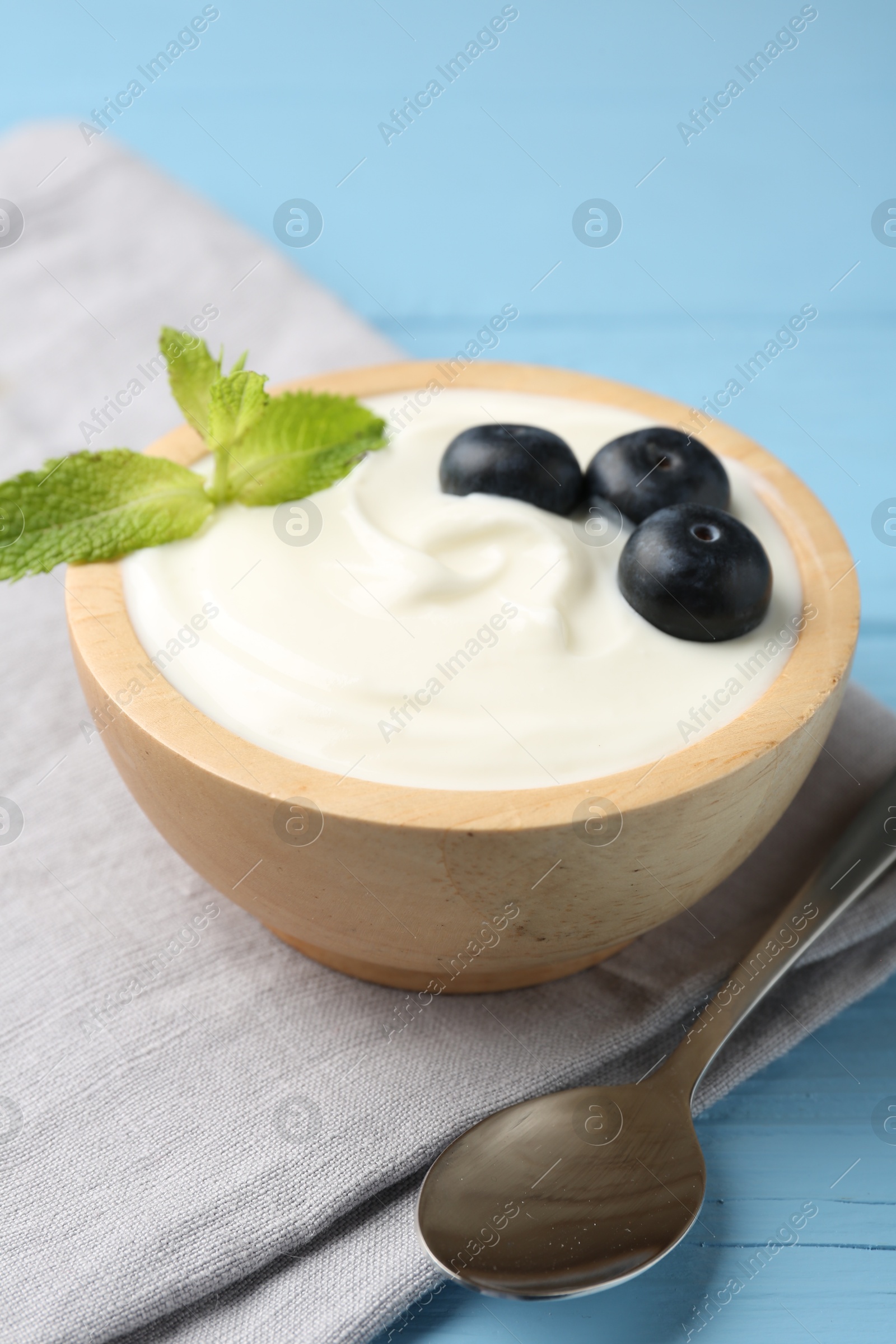 Photo of Tasty yoghurt with blueberries and mint in bowl on light blue wooden table, closeup
