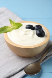 Photo of Tasty yoghurt with blueberries and mint in bowl on light blue wooden table, closeup
