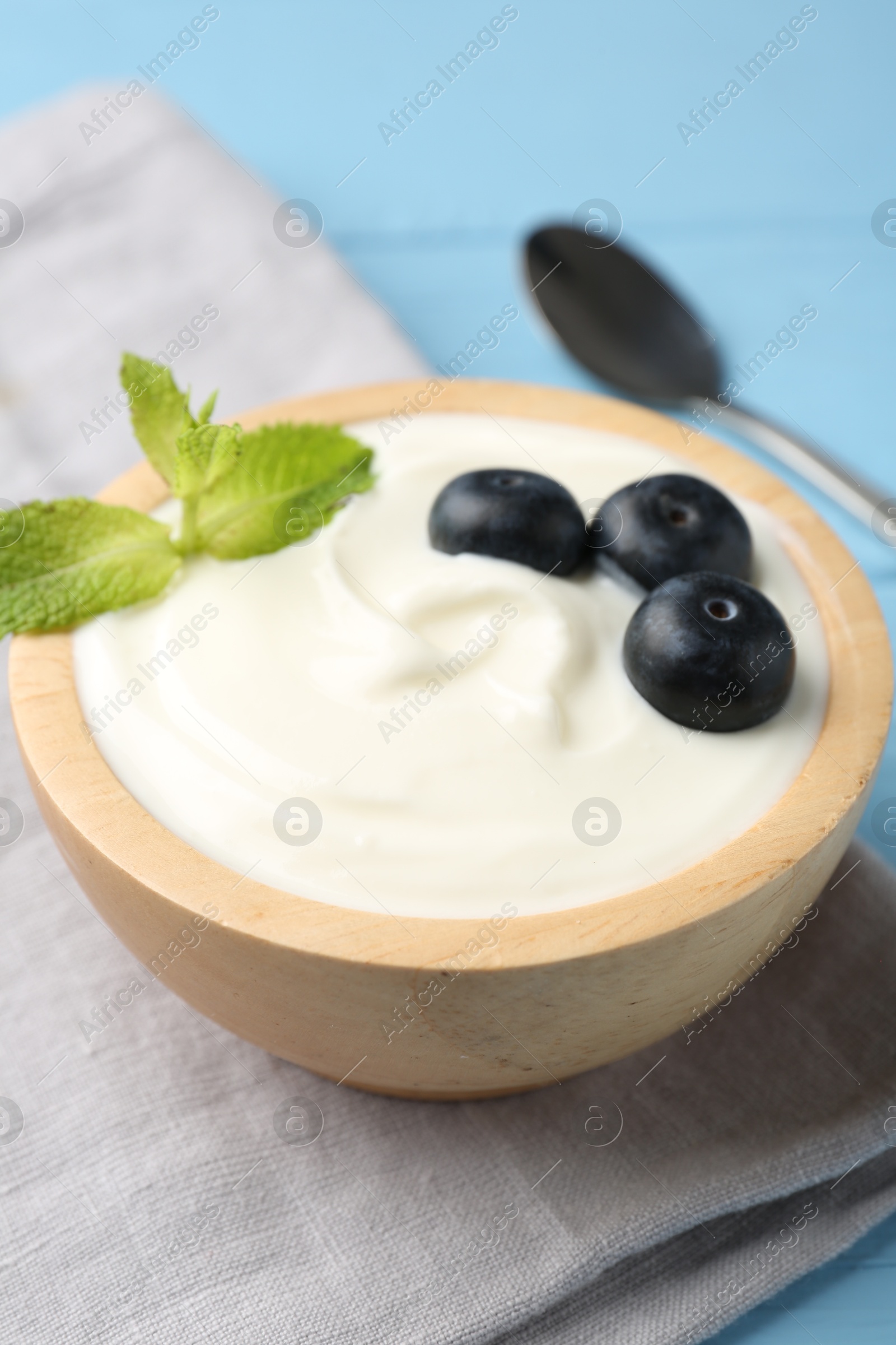 Photo of Tasty yoghurt with blueberries and mint in bowl on light blue wooden table, closeup