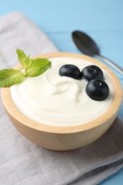 Photo of Tasty yoghurt with blueberries and mint in bowl on light blue wooden table, closeup
