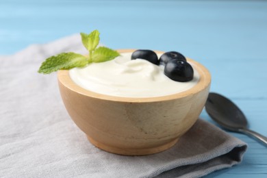 Photo of Tasty yoghurt with blueberries and mint in bowl on light blue wooden table, closeup