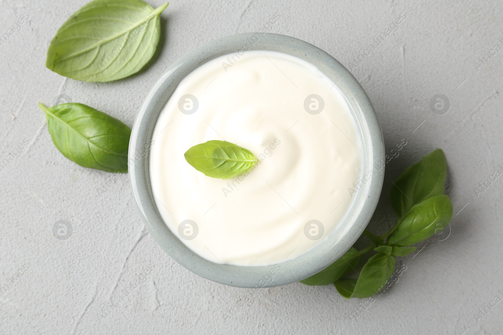 Tasty yoghurt with basil in bowl on light grey table, flat lay Photo of Tasty yoghurt with basil in bowl on light grey table, flat lay