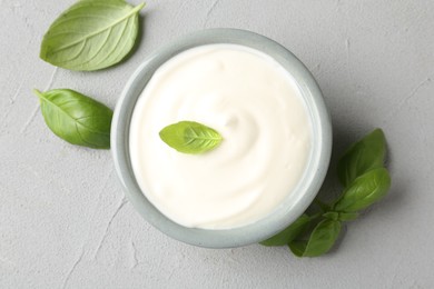Photo of Tasty yoghurt with basil in bowl on light grey table, flat lay