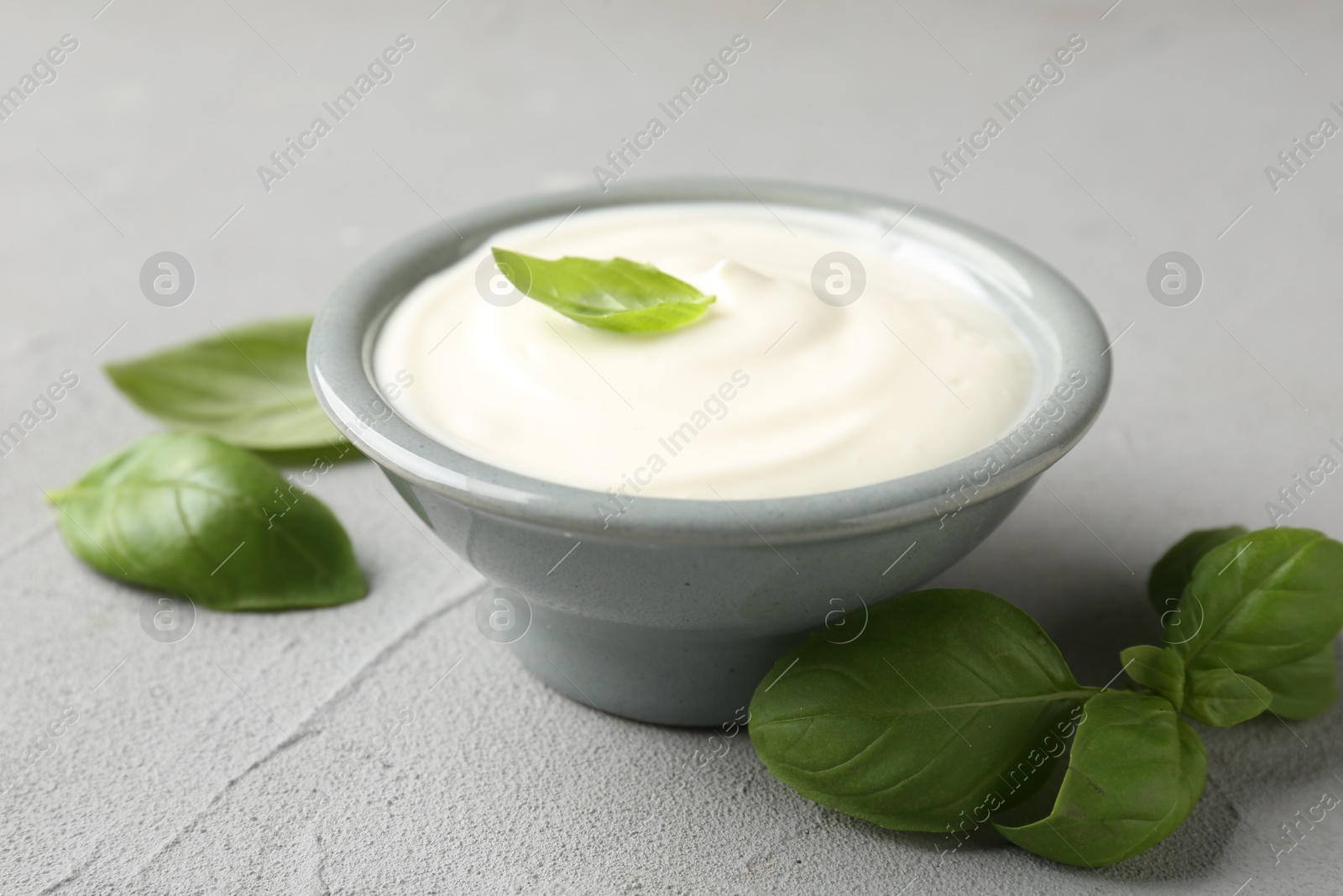 Tasty yoghurt with basil in bowl on light grey table, closeup Photo of Tasty yoghurt with basil in bowl on light grey table, closeup