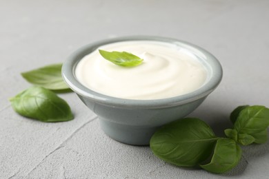 Photo of Tasty yoghurt with basil in bowl on light grey table, closeup