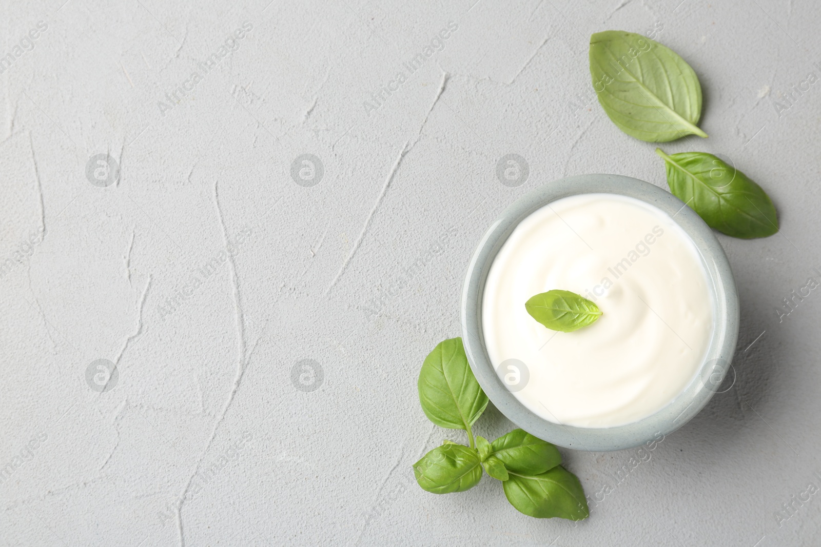 Photo of Tasty yoghurt with basil in bowl on light grey table, flat lay. Space for text
