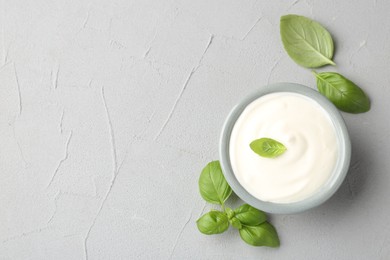 Photo of Tasty yoghurt with basil in bowl on light grey table, flat lay. Space for text