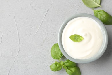 Photo of Tasty yoghurt with basil in bowl on light grey table, flat lay. Space for text