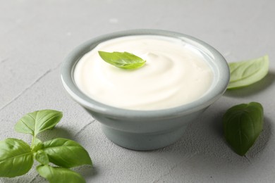 Photo of Tasty yoghurt with basil in bowl on light grey table, closeup