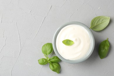 Photo of Tasty yoghurt with basil in bowl on light grey table, flat lay. Space for text