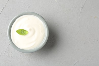 Photo of Tasty yoghurt with basil in bowl on light grey table, top view. Space for text