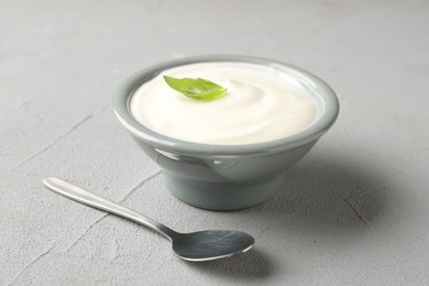 Photo of Tasty yoghurt with basil in bowl on light grey table, closeup