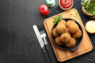 Photo of Delicious fried croquette balls with green onion, parsley, sauces and spices on dark textured table, flat lay. Space for text