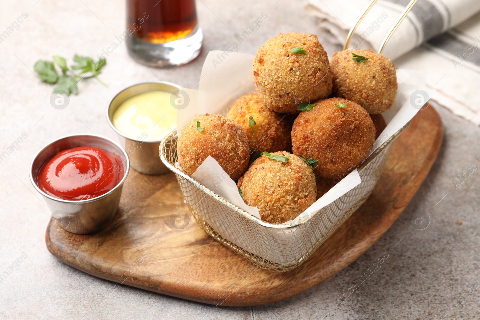 Photo of Delicious fried croquette balls with parsley and sauces on grey textured table, closeup