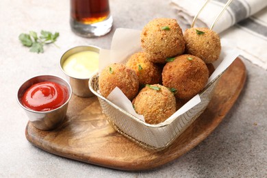 Photo of Delicious fried croquette balls with parsley and sauces on grey textured table, closeup