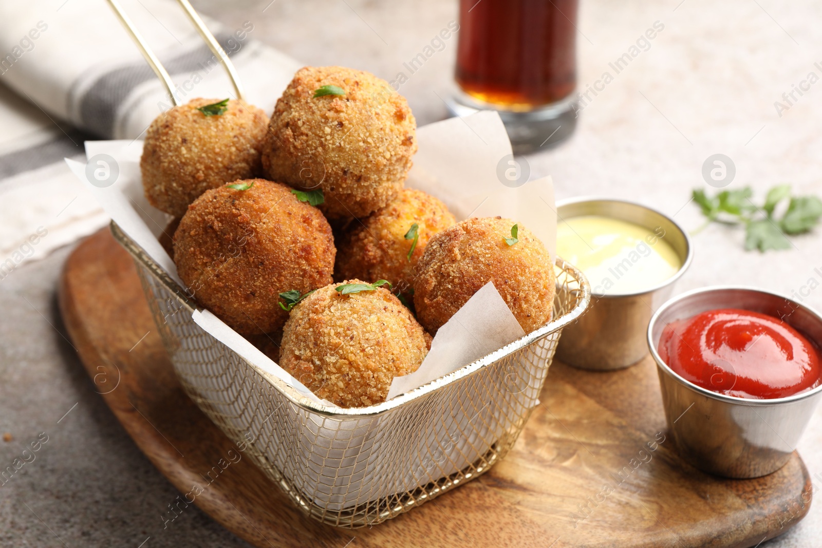 Photo of Delicious fried croquette balls with parsley and sauces on grey textured table, closeup