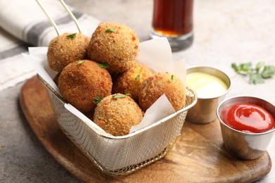 Photo of Delicious fried croquette balls with parsley and sauces on grey textured table, closeup