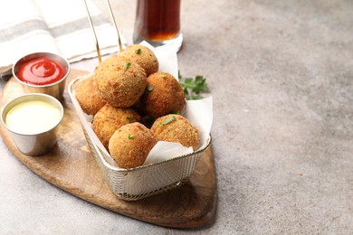 Photo of Delicious fried croquette balls with parsley and sauces on grey textured table, closeup. Space for text