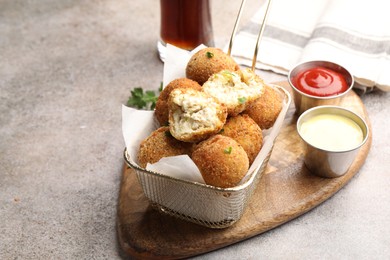 Photo of Delicious fried croquette balls with parsley and sauces on grey textured table, closeup. Space for text