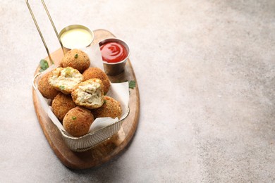 Photo of Delicious fried croquette balls with parsley and sauces on grey textured table, closeup. Space for text