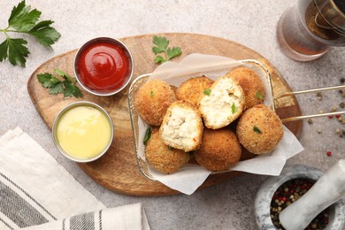 Photo of Delicious fried croquette balls with parsley, sauces and spices on grey textured table, flat lay