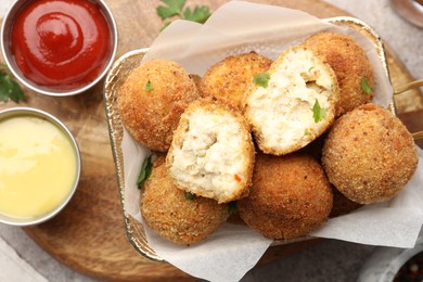 Photo of Delicious fried croquette balls with parsley and sauces on grey textured table, flat lay
