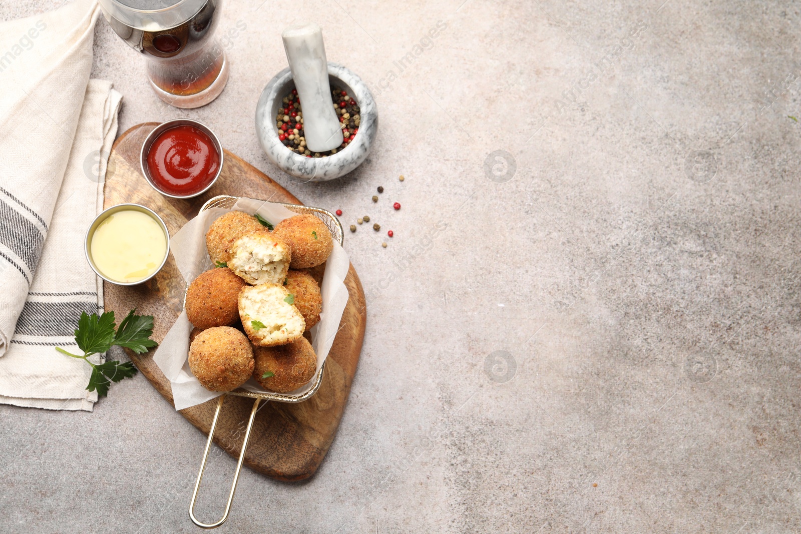 Photo of Delicious fried croquette balls with parsley, sauces and spices on grey textured table, flat lay. Space for text